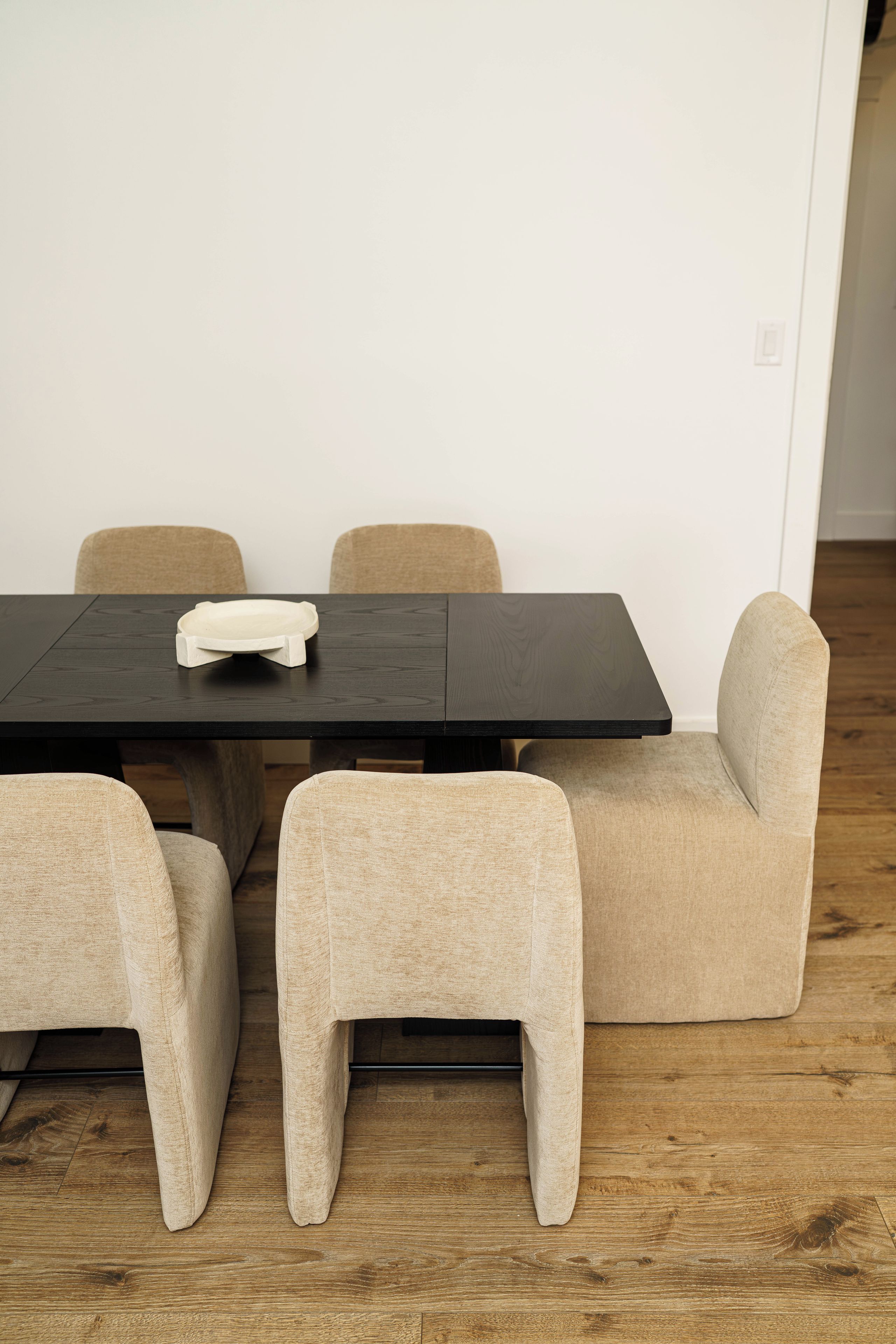 A dining table with four chairs, a white plate, and a wooden floor.