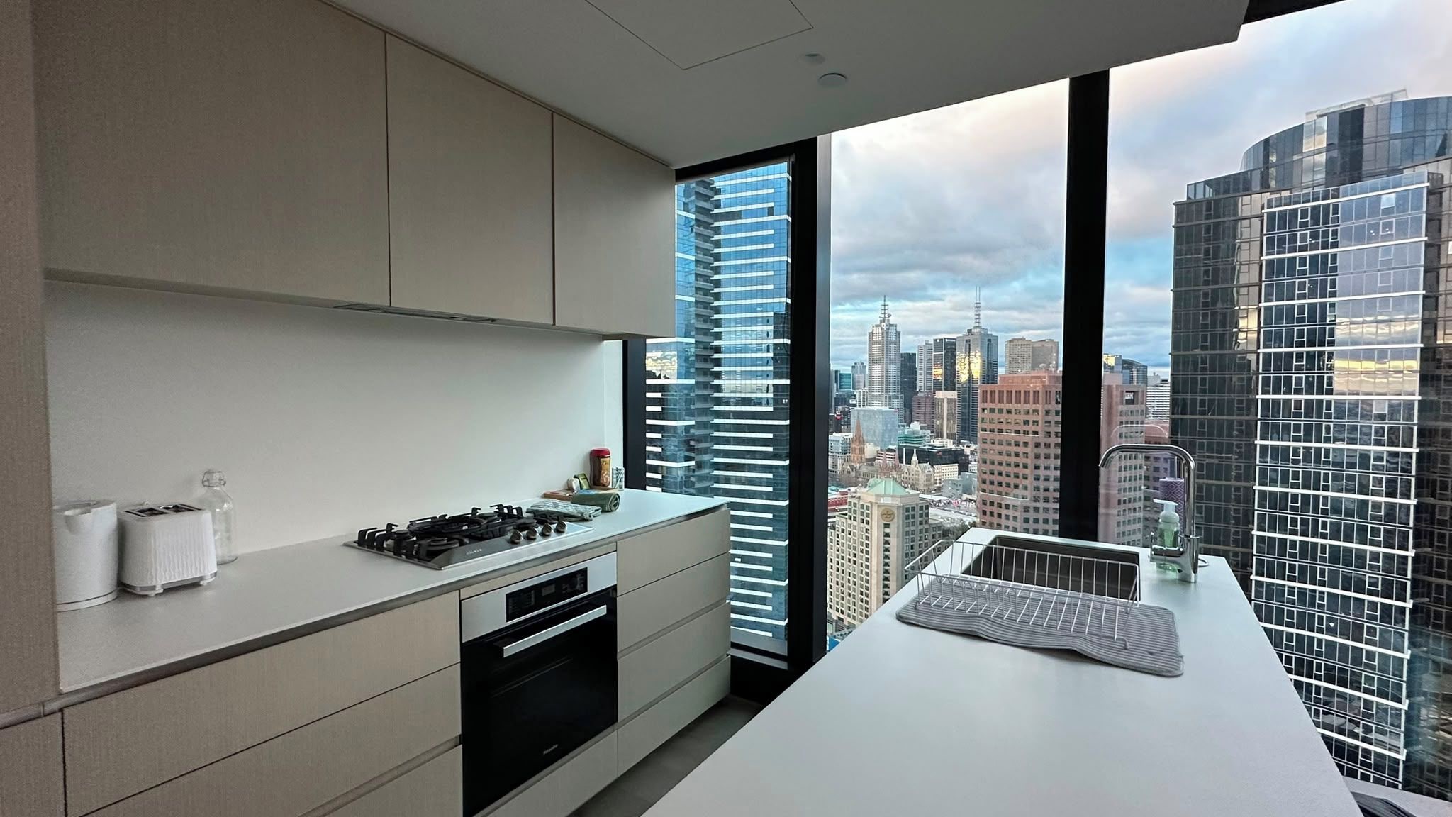 A modern kitchen with a city view, featuring a stove, oven, and a large window.