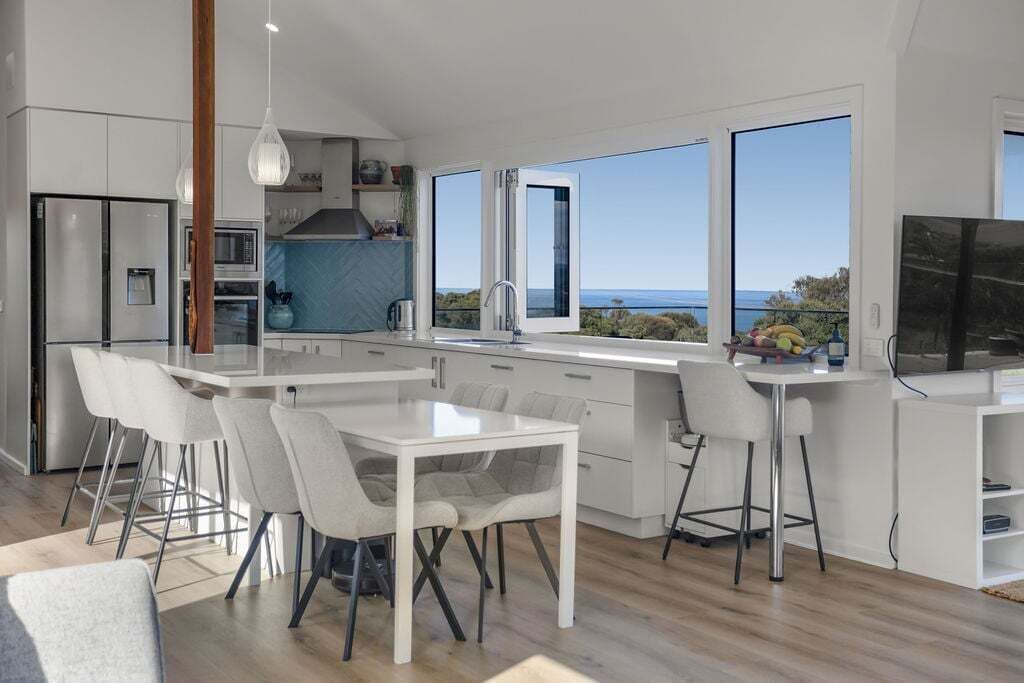Une cuisine moderne dotée d’un grand îlot central, de tabourets de bar et offrant une vue sur la mer.