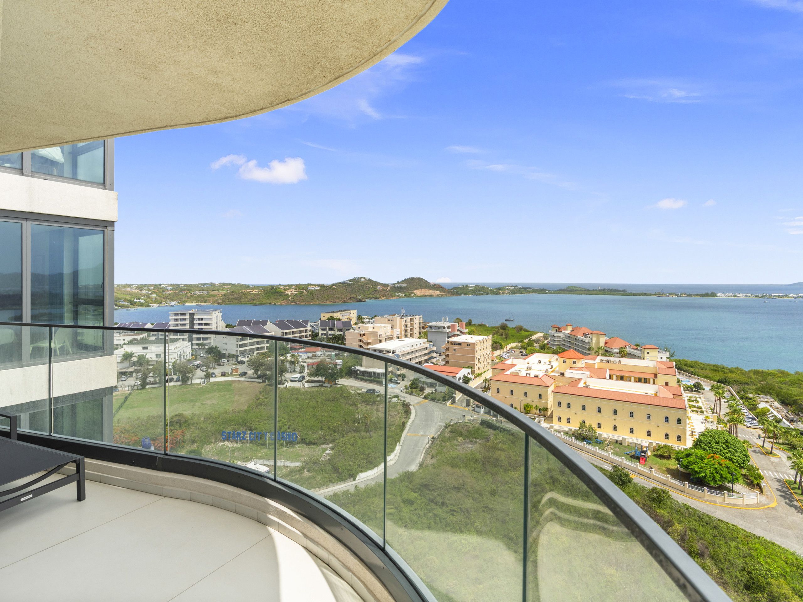 A high-rise building with a glass balcony overlooking a coastal cityscape.
