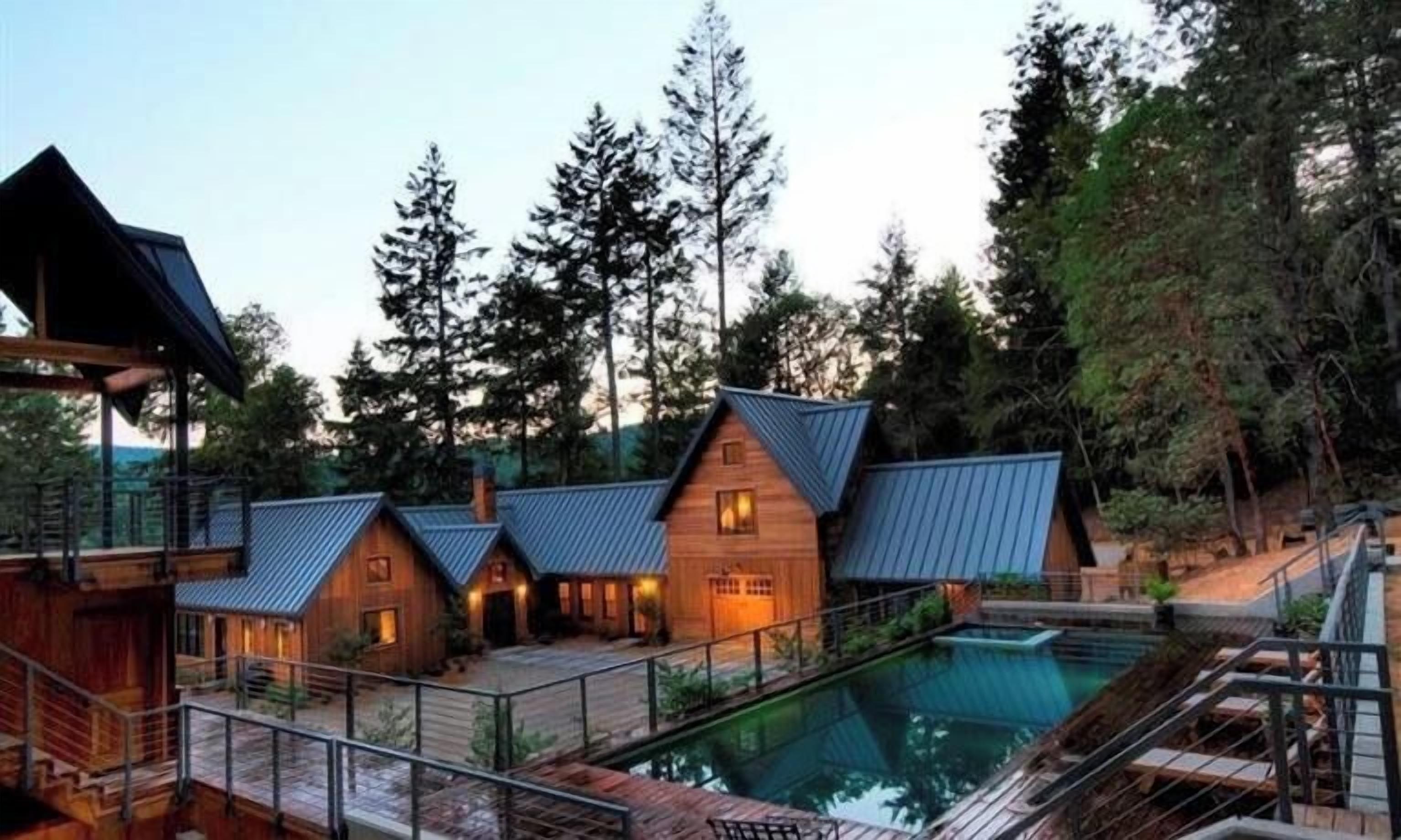 A cabin-style resort with multiple wooden buildings, a swimming pool, and a forested backdrop.