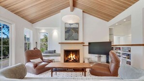 A modern living room with a fireplace, leather sofas, a flat-screen TV, and a large window. - The Ridge at Mill Creek- Hot Tub, Pool & Tastings (Healdsburg)