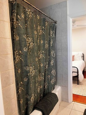 Ein Badezimmer mit Duschvorhang, Badewanne und sichtbarem Durchgang zu einem Schlafzimmer.