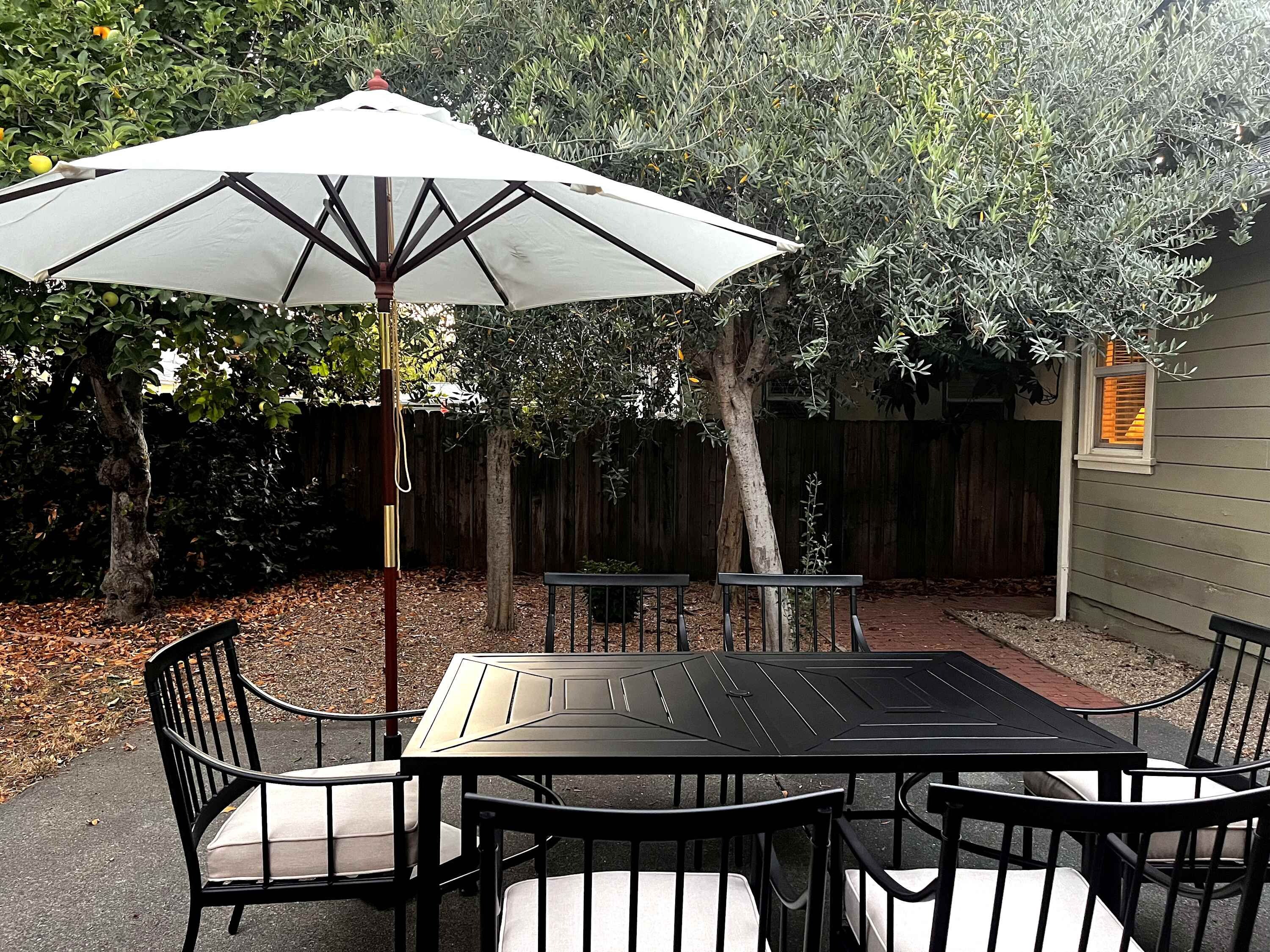 Un patio con una mesa y sillas, una sombrilla y una valla de madera al fondo.