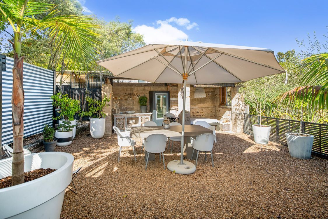 An outdoor patio with a table and chairs, surrounded by potted plants and a large umbrella.