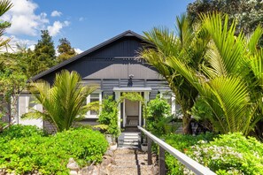 A house with a covered porch, surrounded by lush greenery and a clear sky. - Six and Twenty by Waiheke Pure (Waiheke Island)