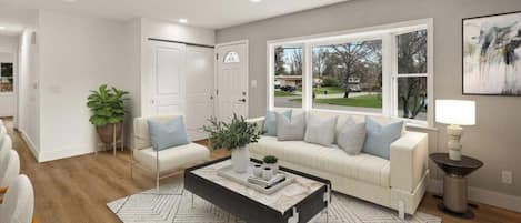 A modern living room with a white sofa, a coffee table, and a large window with a view of a residential area.