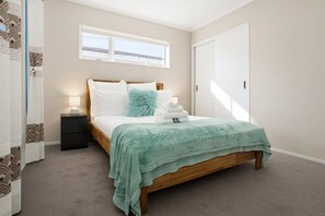 A bedroom with a bed, bedside table, and a window. - Modern 4BR Home | 3 Bath | Free Parking (Papakura)