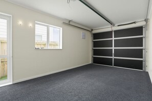 A garage with a grey carpet, a white door, and a black garage door. - Modern 4BR Home | 3 Bath | Free Parking (Papakura)