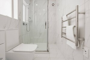 Une salle de bain moderne avec une douche à parois de verre, des toilettes blanches et un porte-serviettes.