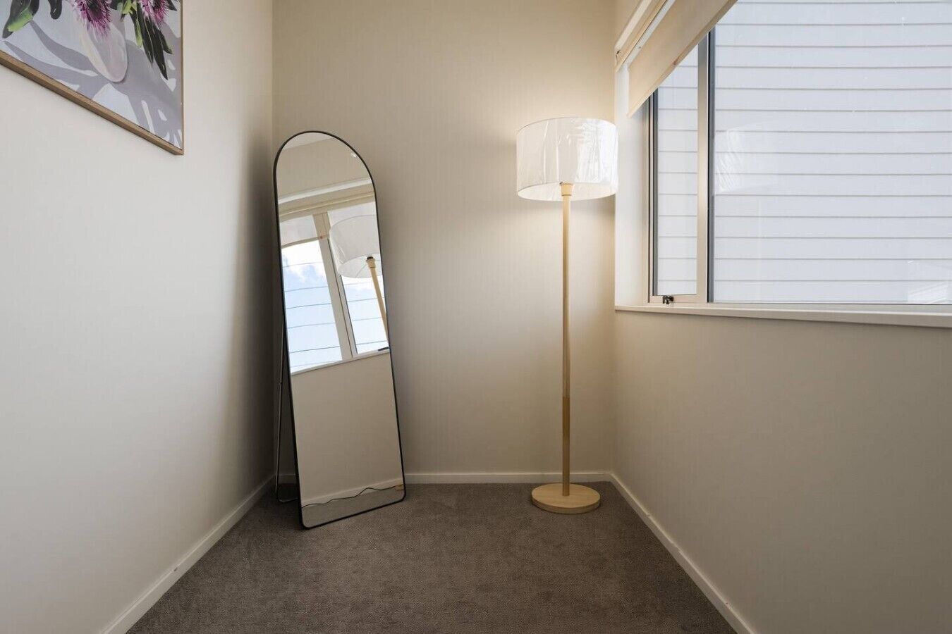 Habitación de esquina con un espejo grande, una lámpara de pie y una ventana con persianas.