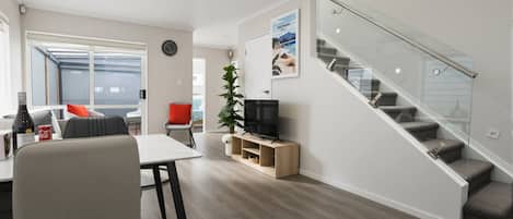 A modern living space with a dining area, a television, a staircase, and a large window.