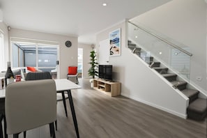Un espace de vie moderne comprenant un coin repas, un téléviseur, un escalier et une grande fenêtre.