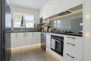 A modern kitchen with white cabinets, stainless steel appliances, and a window providing natural light. - Modern 4BR Home | 3 Bath | Free Parking (Papakura)