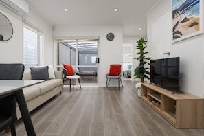 A modern living room with a sofa, chairs, a TV, and a dining area. - Modern 4BR Home | 3 Bath | Free Parking (Papakura)