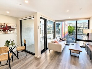 A modern living room with a sofa, a dining table, and a glass partition. - Vibrant 1BR Stay in Braddon | Parking | Near Tram (Braddon)