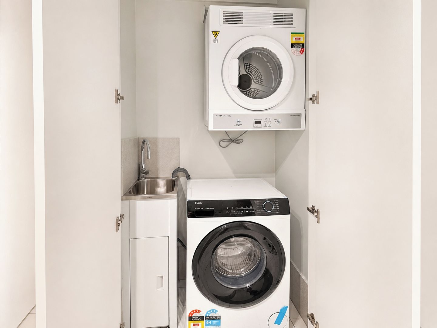 Ein kleiner Hauswirtschaftsraum mit einer Waschmaschine und einem Trockner, einem Edelstahlspülbecken und einem Schrank.