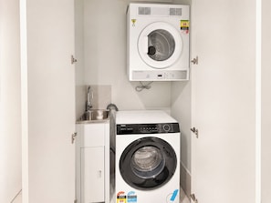 Ein kleiner Hauswirtschaftsraum mit einer Waschmaschine und einem Trockner, einem Edelstahlspülbecken und einem Schrank.