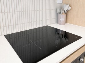 A kitchen with a black induction cooktop, a white countertop, and a utensil holder with spoons. - Vibrant 1BR Stay in Braddon | Parking | Near Tram (Braddon)