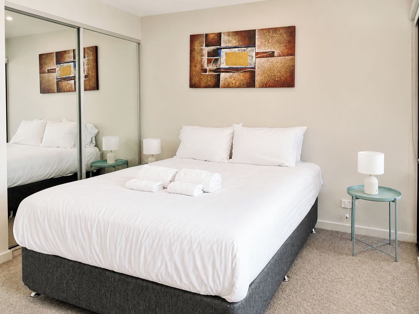 A hotel room with a large bed, a mirror, a painting on the wall, and a small table with a lamp.