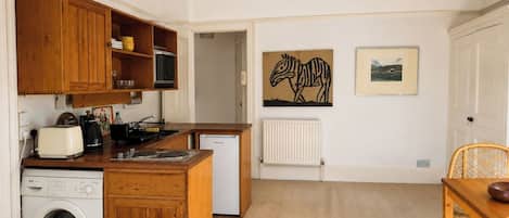 A compact kitchen with wooden cabinetry, a washing machine, a small refrigerator, and a dining area with a table and chairs.
