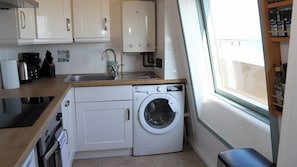 A compact kitchen with a built-in washing machine, a sink, and a window providing natural light.