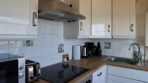 Una cocina moderna con armarios blancos, encimera negra, tostadora integrada, cafetera y pileta de acero inoxidable.