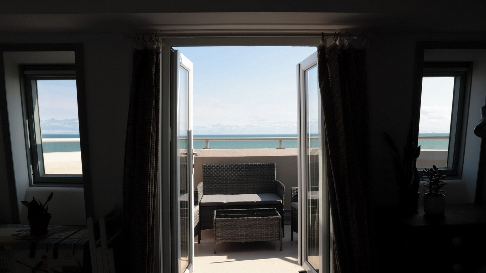 A balcony with a wicker sofa and a small table, overlooking a beach.