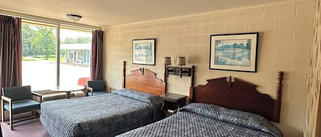 A hotel room with two beds, a chair, a table, and a window with curtains.
