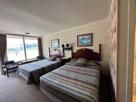 Habitación de hotel con dos camas, un escritorio, una silla y un ventanal con cortinas.