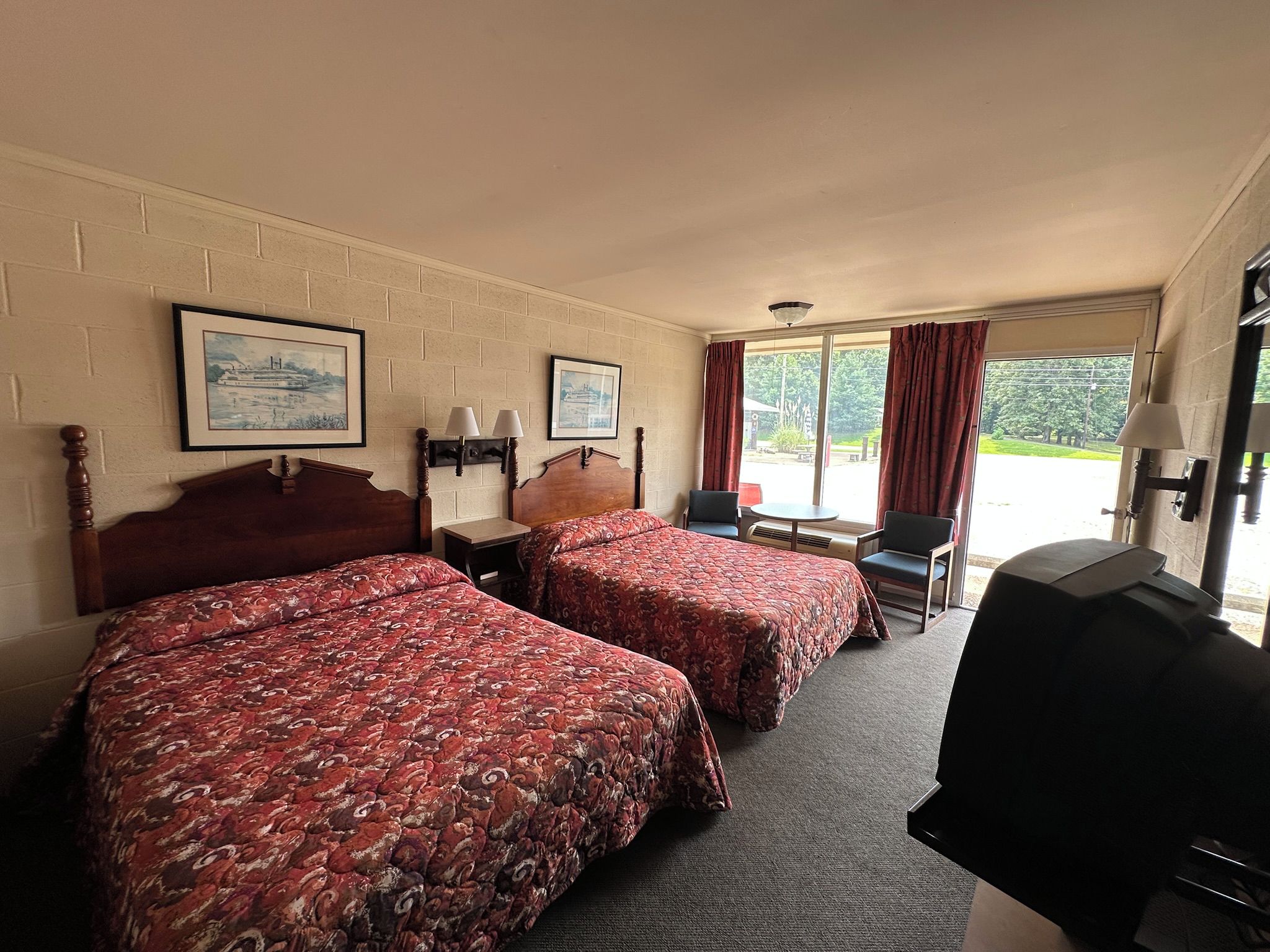 A hotel room with two beds, a desk, a chair, and a television.