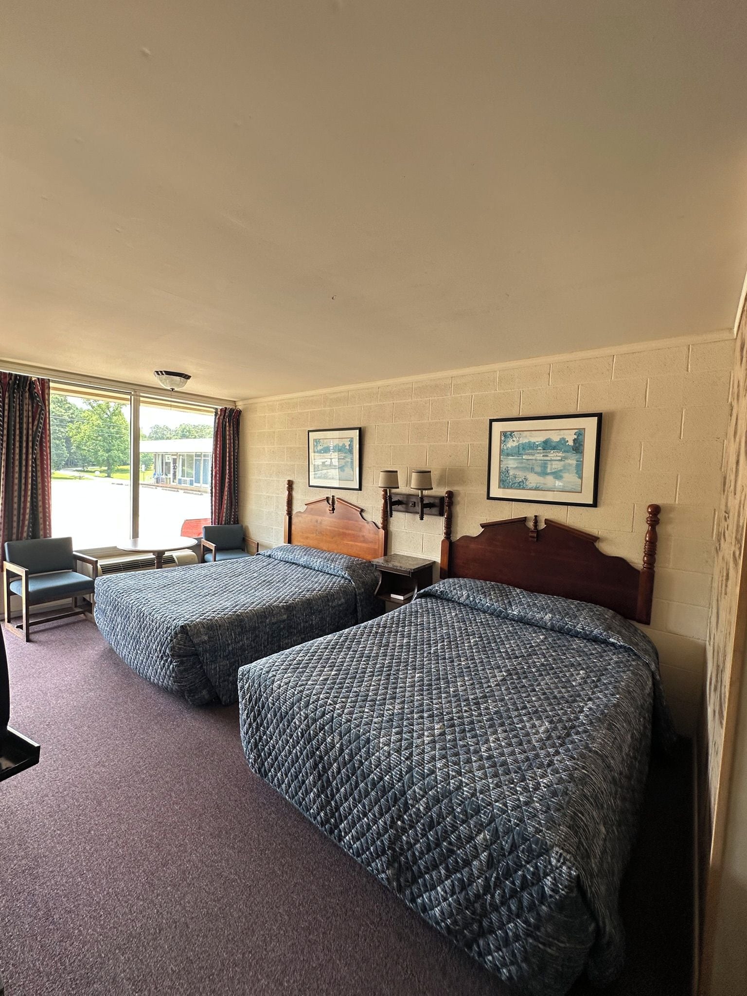 A hotel room with two beds, a chair, a table, and a window with curtains.