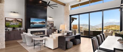 A spacious living room with a fireplace, a large TV, and a dining area with a view of the mountains.