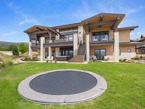Une maison moderne à deux étages, dotée d’une grande pelouse à l’avant et d’un trampoline.