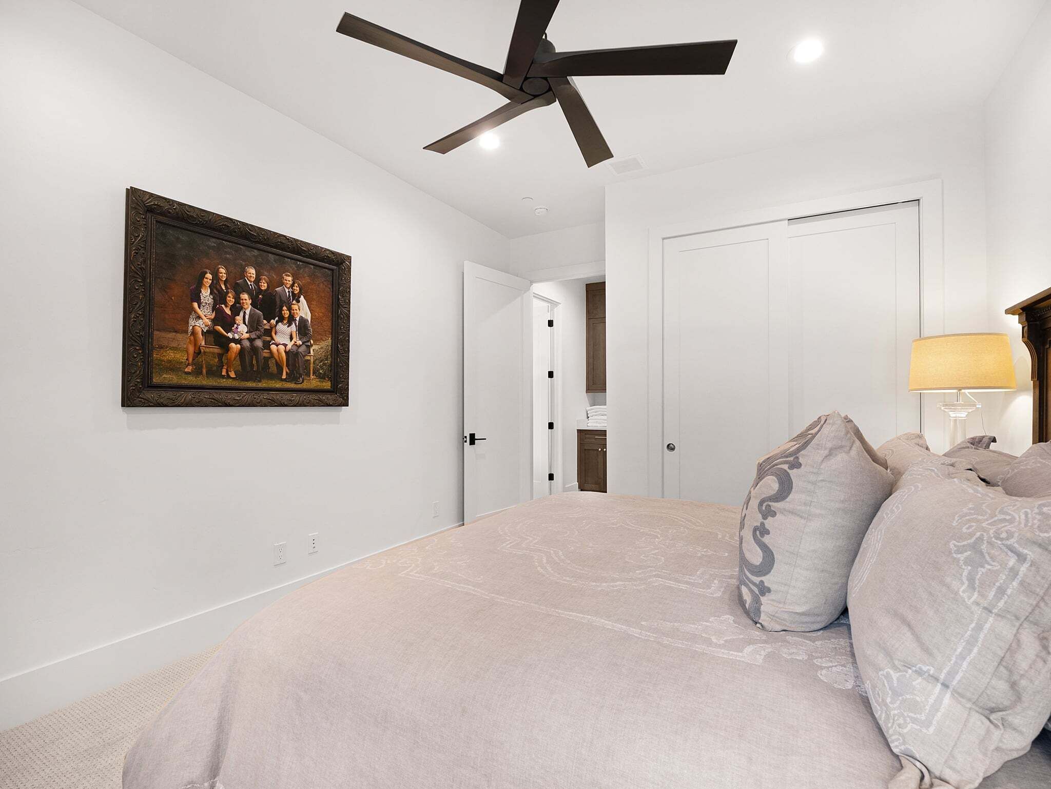 Une chambre à coucher avec un lit, un ventilateur de plafond, une photo de famille encadrée et une porte donnant sur une autre pièce.