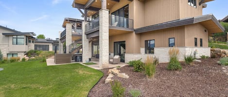 A modern multi-story house with a covered outdoor area, stone pillars, and a landscaped garden.