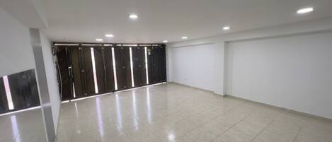 A spacious room with a tiled floor, a door with a black frame, and recessed ceiling lighting.