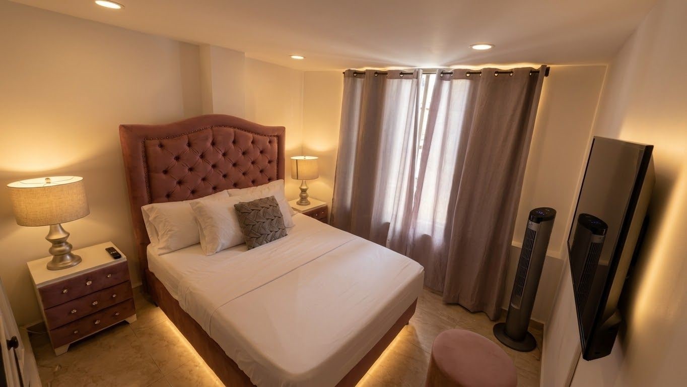 Ein Hotelzimmer mit einem großen Bett, Nachttischlampen, einem Flachbildfernseher und einem Heizlüfter.