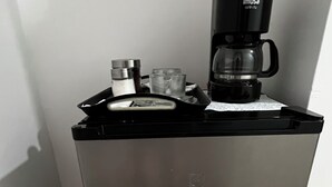 Máquina de café sobre um armário metálico, com uma alavanca, um copo e um recipiente de metal.