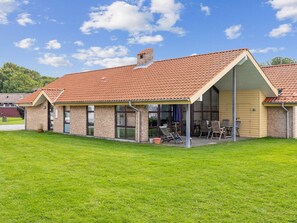 A single-story building with a red-tiled roof, a covered patio area with chairs, and a grassy lawn. - 8 Person Holiday Home in Egernsund (Broager)