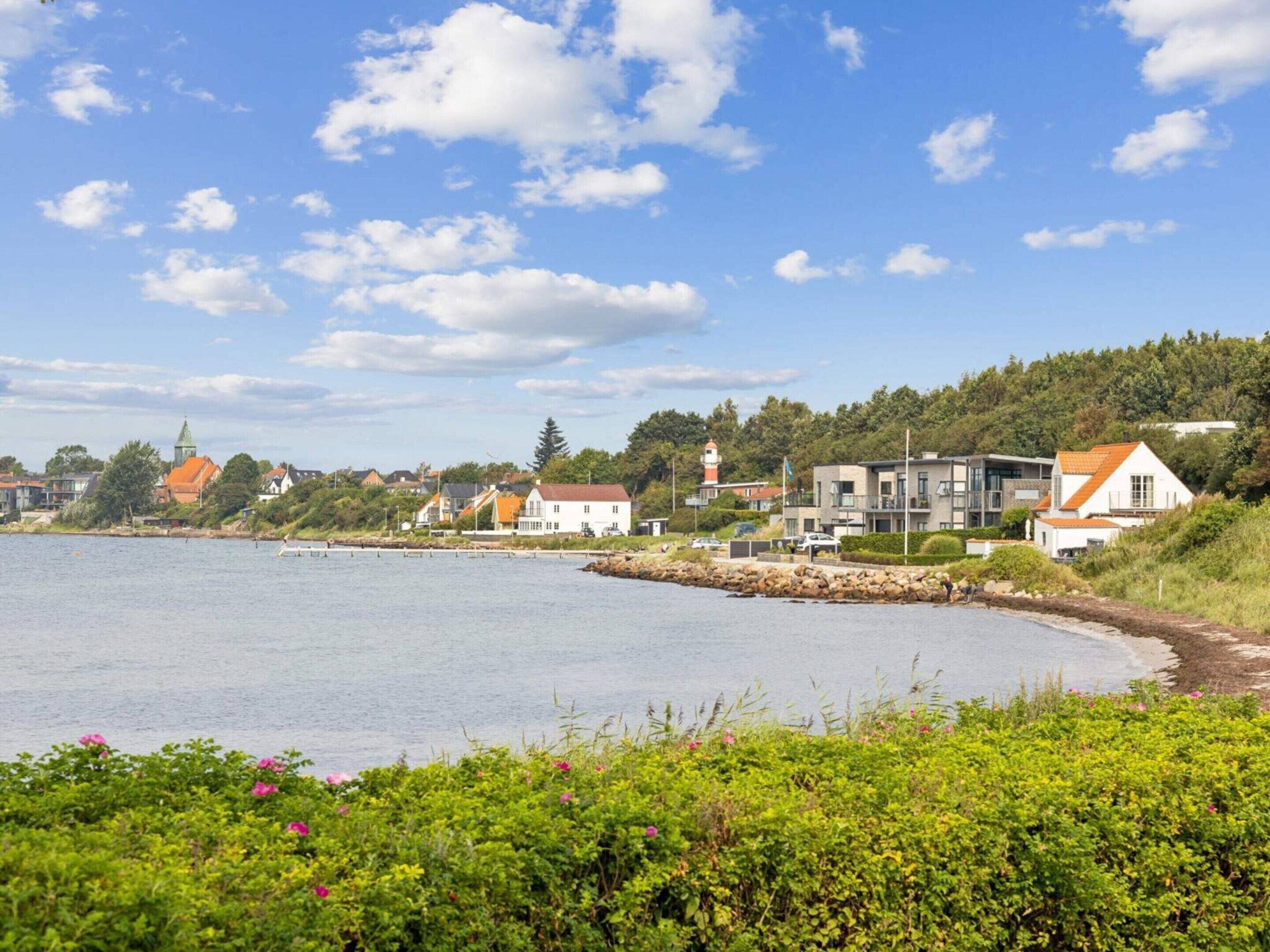 A coastal town with modern houses, a lighthouse, and a calm sea.