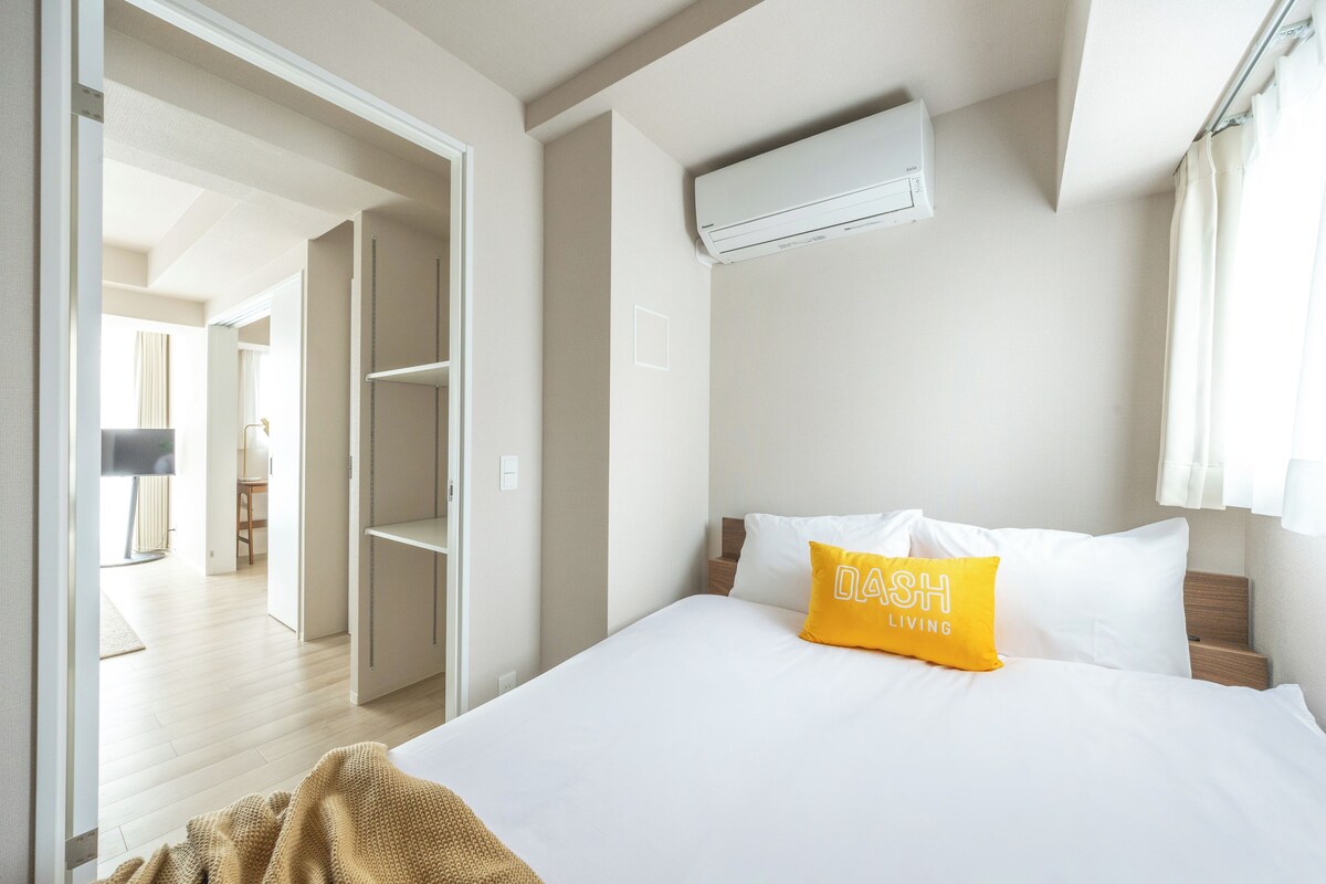 Habitación de hotel con cama, almohada amarilla, unidad de aire acondicionado blanca y vista a un pasillo.