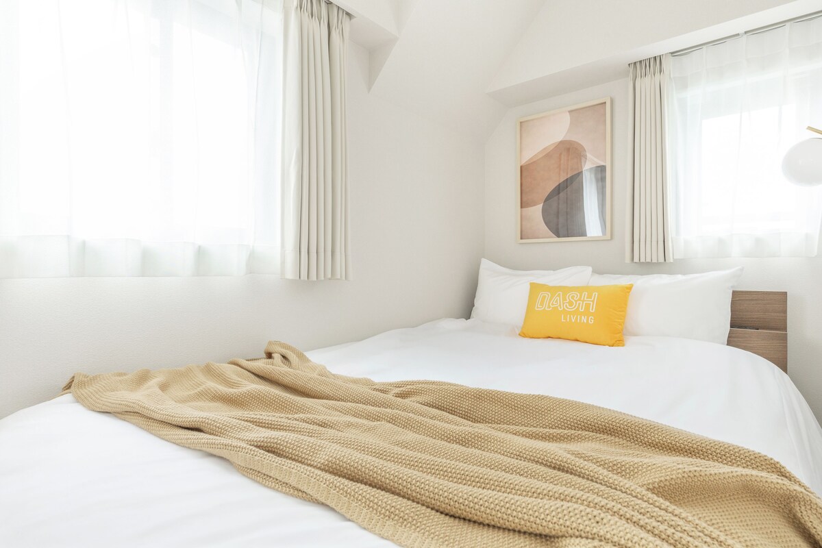 Un dormitorio con cama, un almohadón amarillo, una manta color beige y un cuadro en la pared.