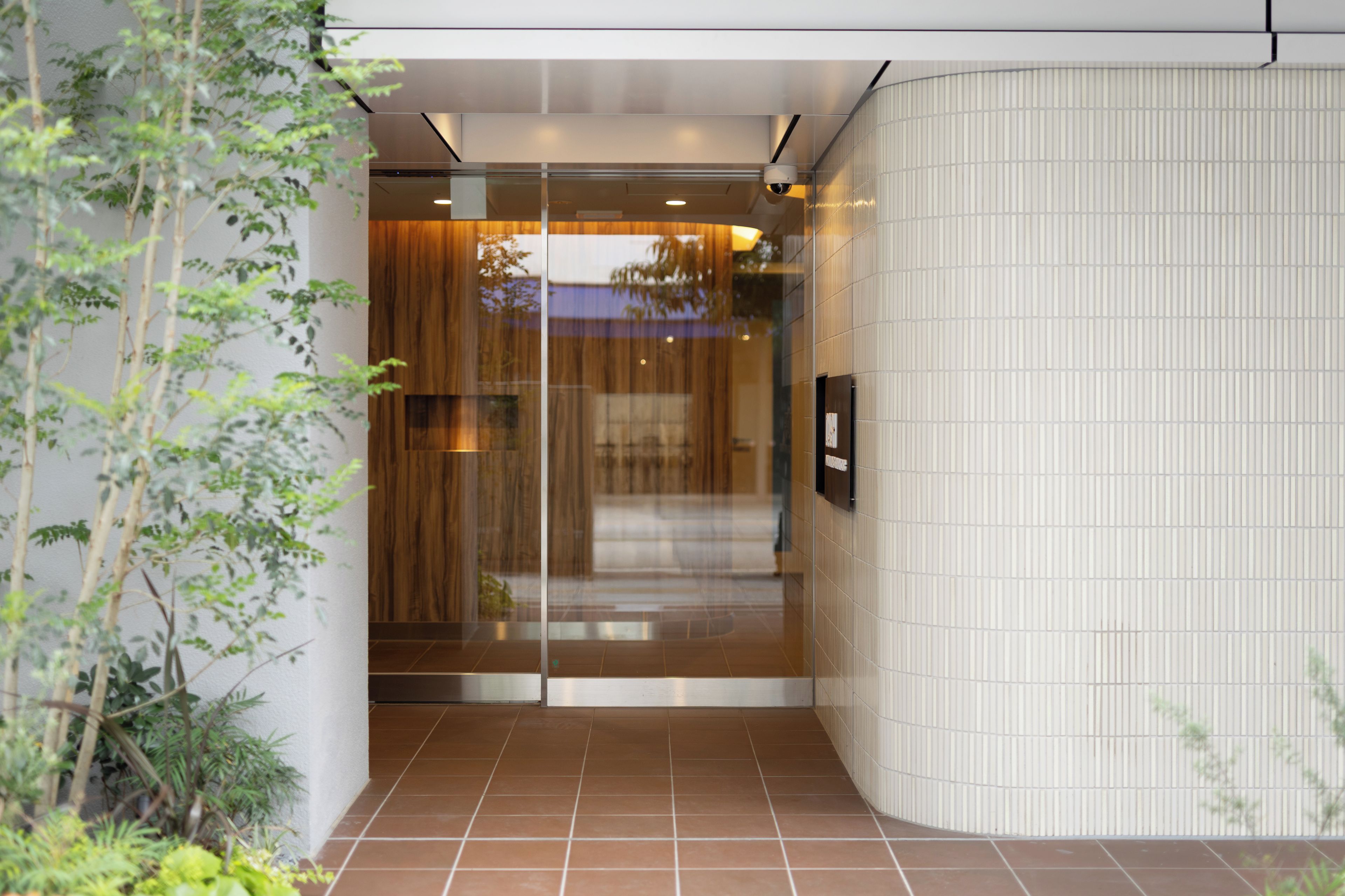 A modern building entrance with a glass door, a tiled floor, and a security camera.