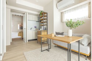 Un espacio de estar moderno y luminoso con una mesa de comedor de madera, un sofá y una zona de cocina con estantes abiertos.