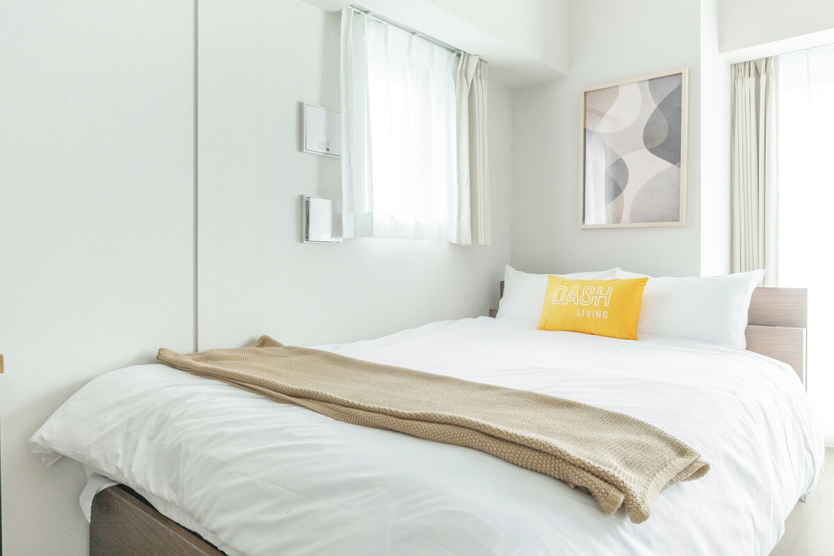 Habitación de hotel con cama, ventana con cortinas, aire acondicionado de pared y un cuadro abstracto enmarco.