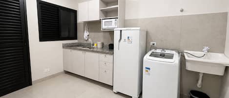 Una cocina compacta con armarios blancos, microondas integrado, refrigerador, lavadora y un lavamanos.