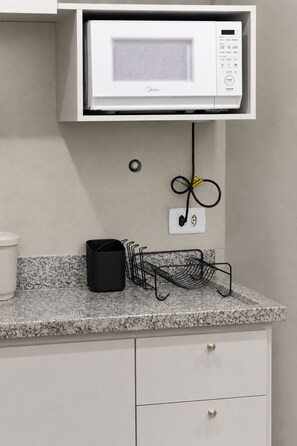A kitchen with a microwave, a power outlet, and a metal rack on the countertop.