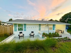 A single-story house with a porch, two chairs, and a string of lights. - Hibiscus Hideaway - Coastal Retreat by the Beach (Ormond Beach)