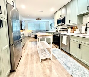 A modern kitchen with stainless steel appliances, a wooden table, and light-colored cabinetry. - Hibiscus Hideaway - Coastal Retreat by the Beach (Ormond Beach)